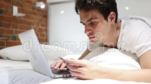 为成功的网上购物交易而兴奋的床上男人视频的预览图