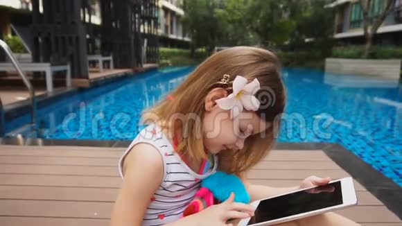 小女孩在游泳池附近玩平板电脑和玩具视频的预览图