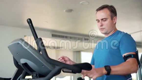 适合年轻人在健身房做运动的天鹅绒模拟器智能手机带耳机听音乐视频的预览图