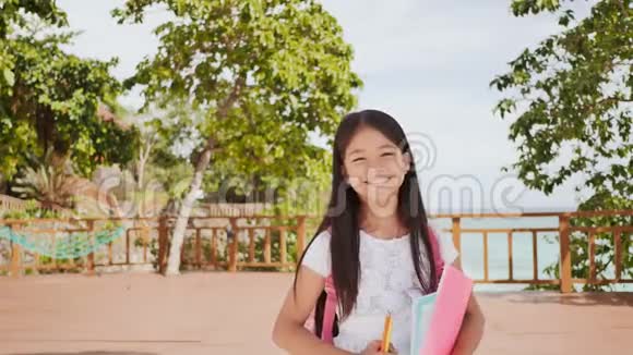 一个迷人的菲律宾女学生带着背包和书在海岸外的公园里一个女孩高兴地摆姿势举起她视频的预览图