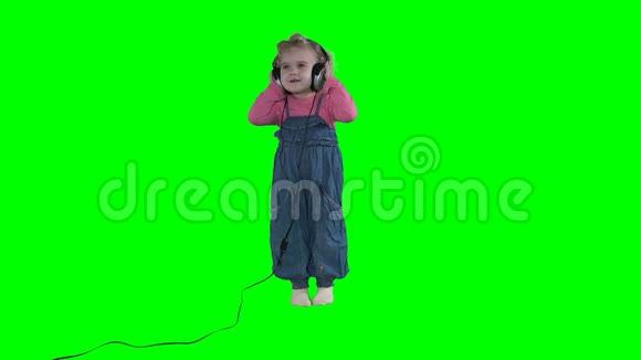 带着大耳机在绿色背景下听音乐的幼儿女孩视频的预览图