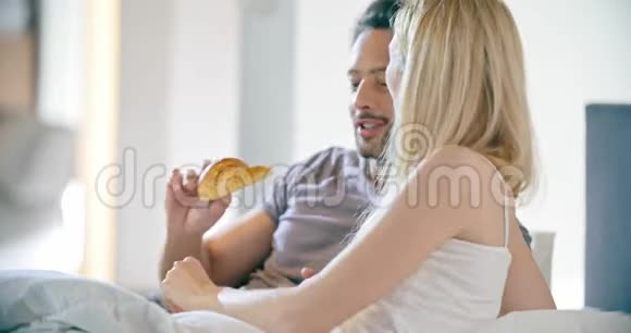 美丽的男人和女人在床上吃早餐恋爱中的情侣早晨在卧室的家里醒来视频的预览图