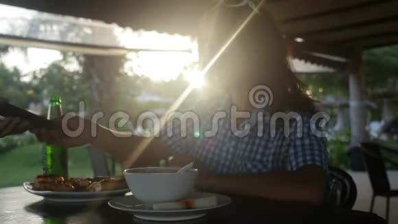 年轻女性在日落时喝啤酒在户外咖啡馆使用手机并有镜头闪光效果3840x2160视频的预览图