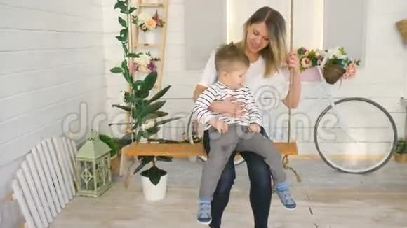 快乐的年轻母亲和她的小儿子坐在秋千上一起在卧室里玩耍视频的预览图