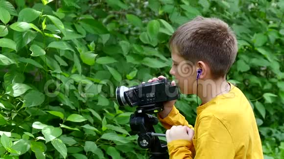 小男孩看着绿色公园慢动作背景下的摄像机视频的预览图