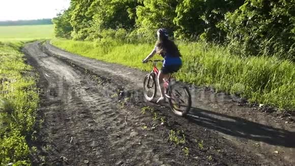 日落时分年轻女孩骑自行车在乡村公路上视频的预览图