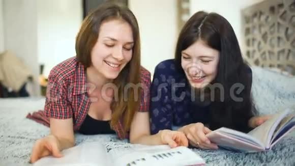 两个年轻的女朋友在家里卧室的床上看杂志视频的预览图