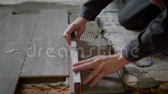 在铺设瓷砖的过程中检查瓷砖表面水平的人的手的特写镜头视频的预览图