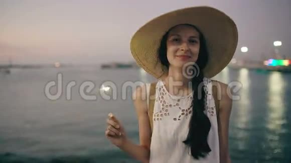 年轻漂亮的女孩戴着帽子在日落时分在海滩上闪闪发光视频的预览图