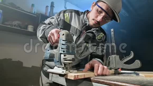 一个留着灰色工作服和护目镜的年轻人一个木匠在家里做电锯视频的预览图