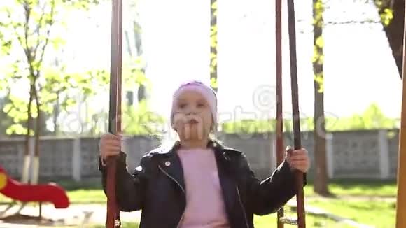 小女孩在城市公园荡秋千快乐的孩子在荡秋千穿粉红色衣服的概念女郎在秋千上快速挥舞视频的预览图