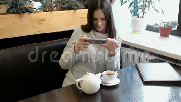 年轻的女人深色的照片茶壶和杯在一家咖啡馆在她的手机前景视频的预览图