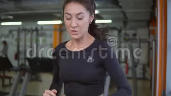 在跑步机上跑步健身房里的一个漂亮的运动黑发女人视频的预览图