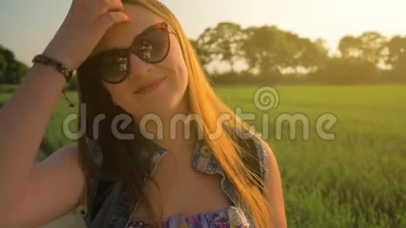 美丽的年轻女孩直长发在风中发展日落时站在田野里慢动作视频的预览图