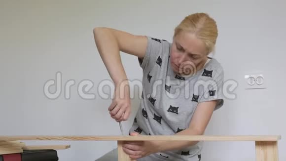 一个女人坐在地板上收集房间里的木制家具用螺丝刀拧螺丝视频的预览图