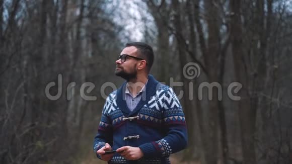 戴眼镜的人正穿过秋天的森林用智能手机拍照慢动作视频的预览图