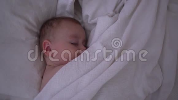 一个可爱的睡着的婴儿躺在白色毯子下慢动作视频的预览图