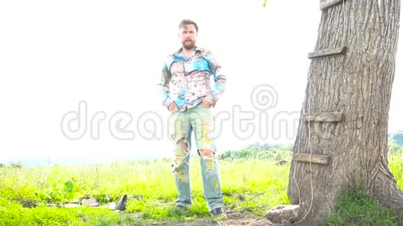 一个英俊的长胡子的人正靠在田野里的树上视频的预览图
