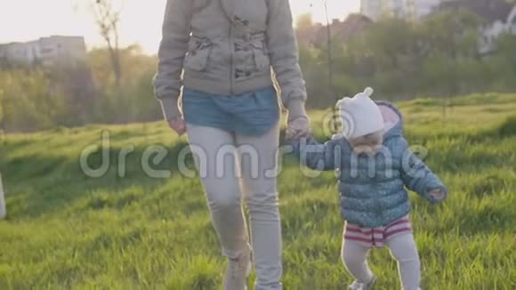 在阳光明媚的春天妈妈和蹒跚学步的女儿在公园里牵着手视频的预览图