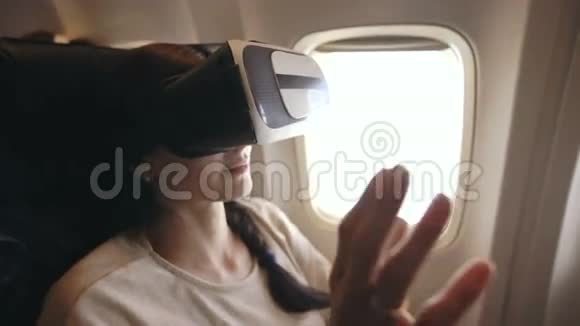 年轻的女游客在飞机飞行过程中放松使用VR耳机智能手机视频的预览图