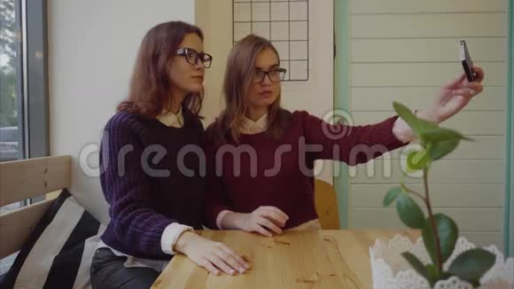 两个漂亮的女孩摆姿势准备在室内咖啡厅自拍视频的预览图