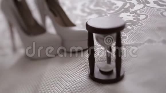 由白色高跟鞋后面的老式沙漏组成的婚礼构图的特写视频的预览图