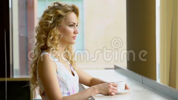 美丽的金发女孩在咖啡馆喝一杯热咖啡或茶视频的预览图