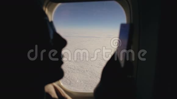 在飞行过程中使用手机坐在飞机窗口附近的特写剪影女士视频的预览图