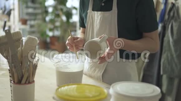 艺术家用白色油漆在陶瓷杯上画一支刷子视频的预览图