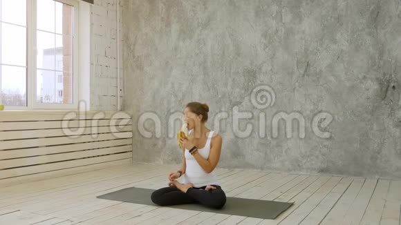 可爱的年轻女人一边吃香蕉一边坐在运动垫上视频的预览图