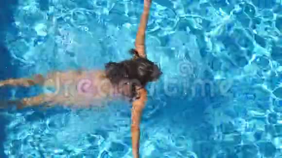 无法辨认的美丽女孩飘过酒店的游泳池年轻女子在清水盆里游泳视频的预览图