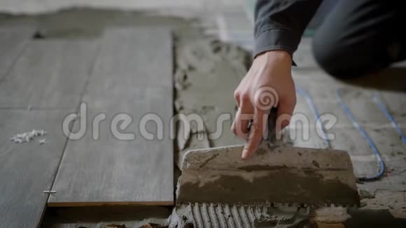 在安装瓷砖的过程中大师手拿着有牙齿的铲子在地板上均衡建筑砂浆视频的预览图