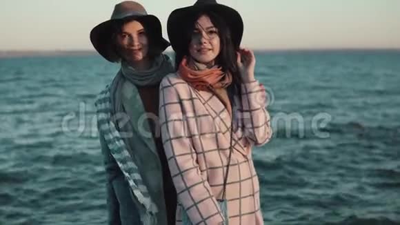 秋海背景下日落时戴着帽子和外套的迷人女孩的肖像朋友们花在户外视频的预览图
