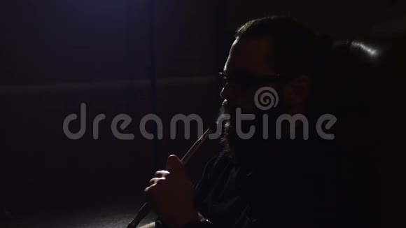 戴眼镜的小胡子男子抽着一根钩在黑色背景上慢慢地用4k的速度吹出烟雾特写视频的预览图