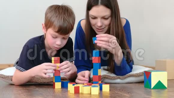 从街区建造一座塔妈妈和儿子一起玩的木制彩色教育玩具积木躺在地上视频的预览图