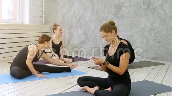 女性在健康俱乐部练习瑜伽年轻女孩在健身后聊天和放松瑜伽教练使用智能手机视频的预览图