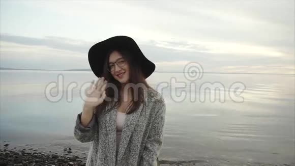 日落时分戴着黑色帽子和眼镜的年轻漂亮女子在海边露着大拇指视频的预览图