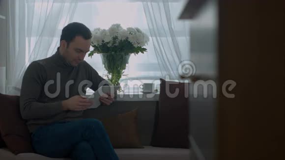 年轻人在沙发上用平板电脑上网视频的预览图