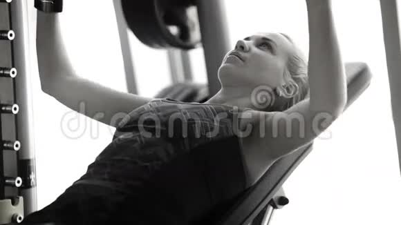 一位女士在健身房锻炼举起杠铃的黑白镜头视频的预览图