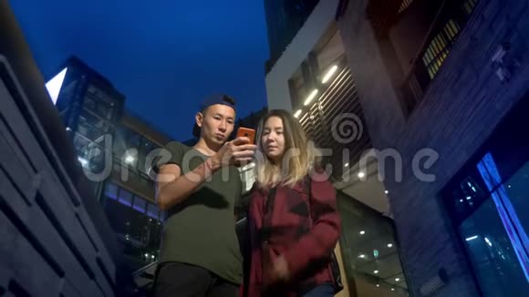 快乐的年轻亚洲夫妇的男朋友和女朋友晚上站在城市街道上使用智能手机视频的预览图