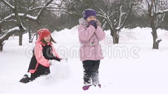 快乐的孩子们在雪地里玩耍的慢动作两个快乐的女孩在冬天外面玩视频的预览图