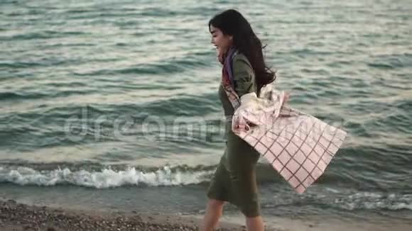 日落时穿着秋衣的年轻女子沿着海岸散步慢动作视频的预览图