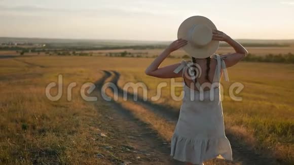 日落时分戴着帽子和裙子的女孩在田野上视频的预览图