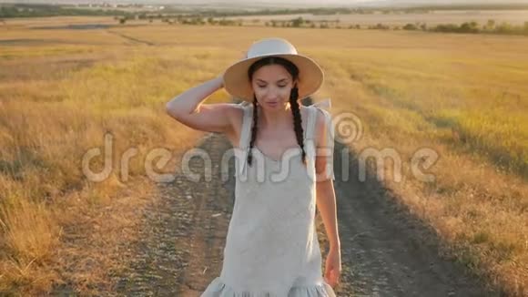 日落时分戴着帽子和裙子的女孩在田野上视频的预览图