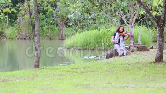 一个亚洲女人在湖边拉小提琴视频的预览图