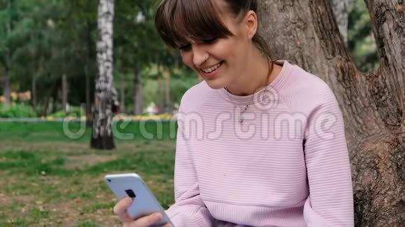 照片中年轻的白人美女微笑着穿着粉色运动衫在智能手机上聊天视频的预览图