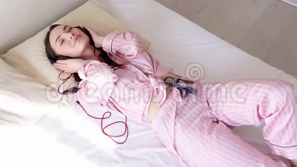穿着睡衣的女人躺在床上用耳机随着音乐跳舞视频的预览图