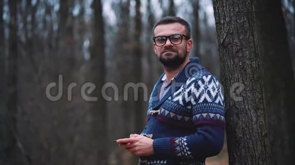 戴眼镜的人正穿过秋天的森林使用智能手机视频的预览图