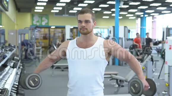 年轻的肌肉男在健身房用哑铃做运动健身馆男性健美运动员的肖像视频的预览图