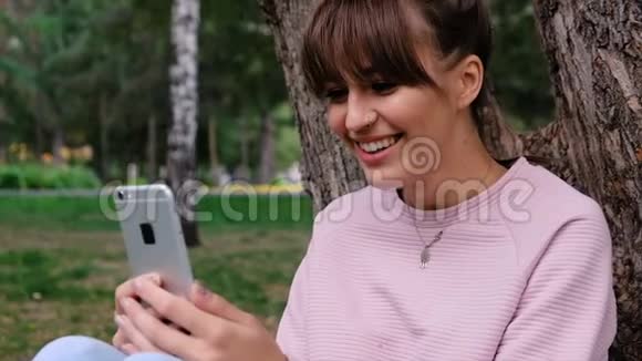 照片中年轻的白人女孩微笑着穿着粉色运动衫在智能手机上聊天视频的预览图